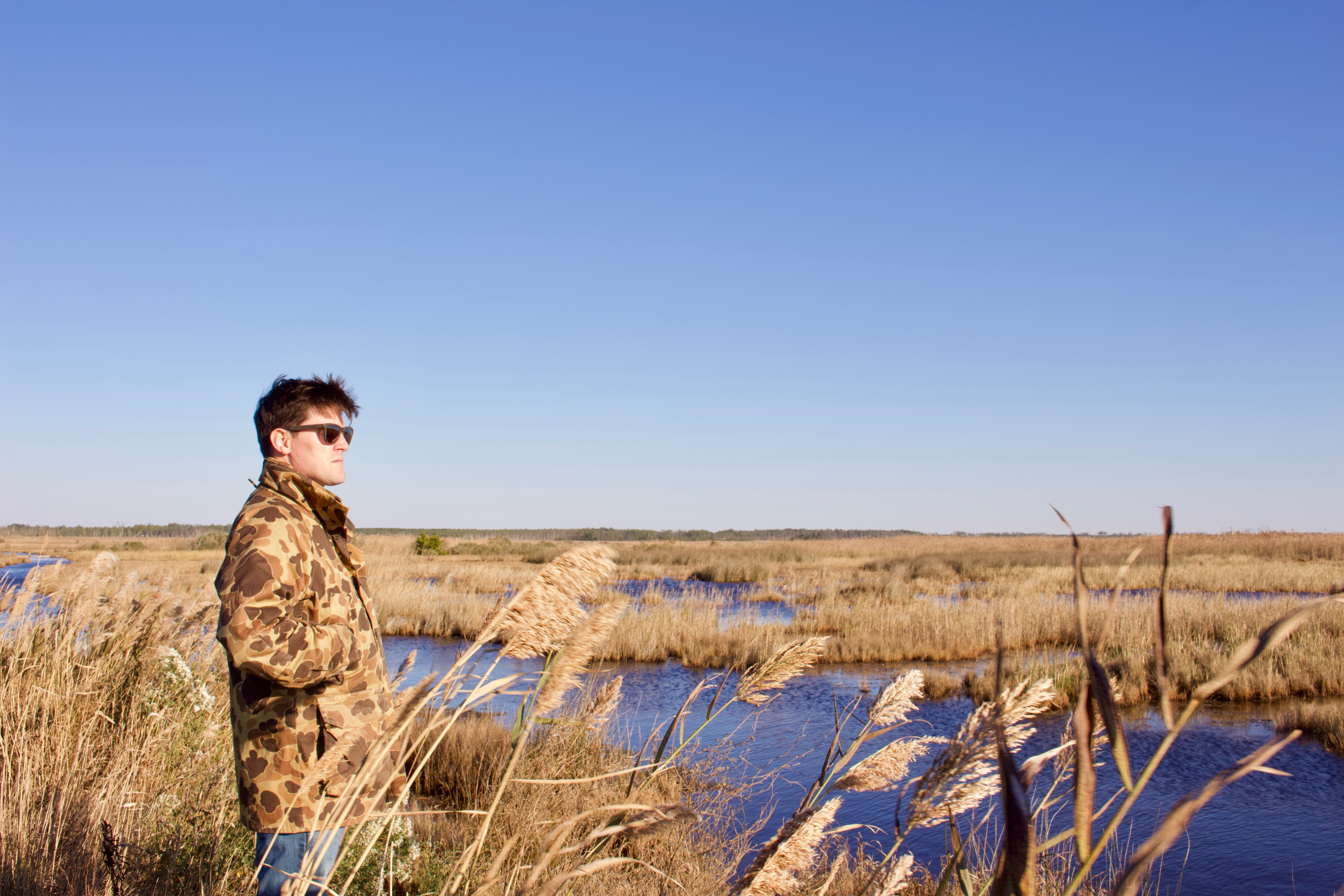 Man in camouflage jackets overlooks a marsh